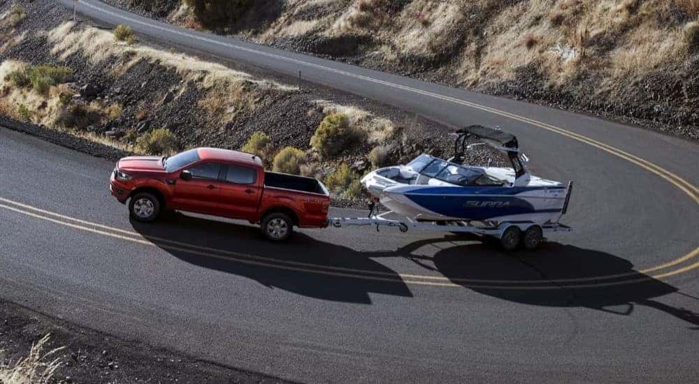 A red 2023 Ford Ranger XLT towing a boat up a winding mountain road.