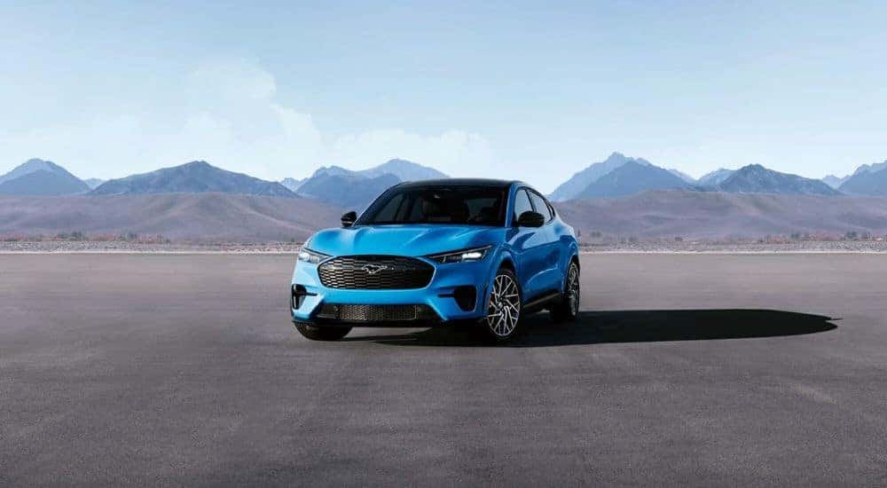A blue 2024 Ford Mustang Mach-E is shown on pavement after looking at electric vehicles for sale.