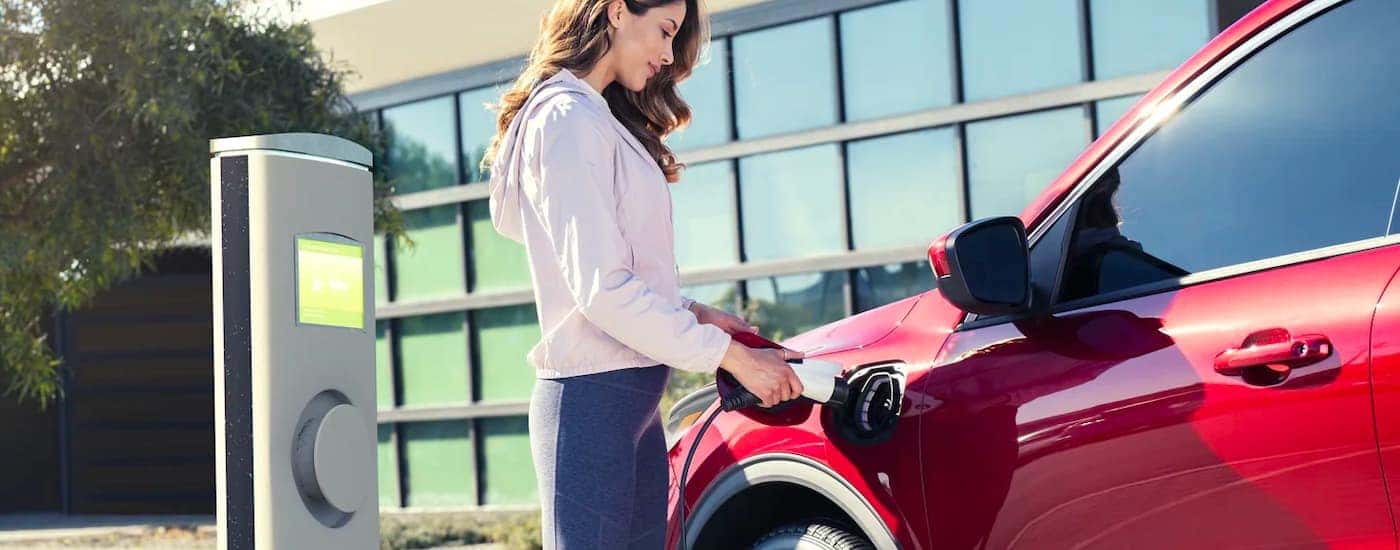 A woman inserting a charging plug into a red 2023 Ford Escape Hybrid parked outside of a building.