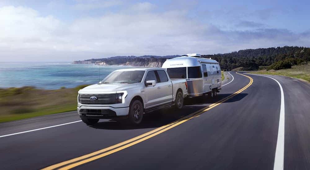 A white 2025 Ford F-150 Lightning is shown towing a trailer.