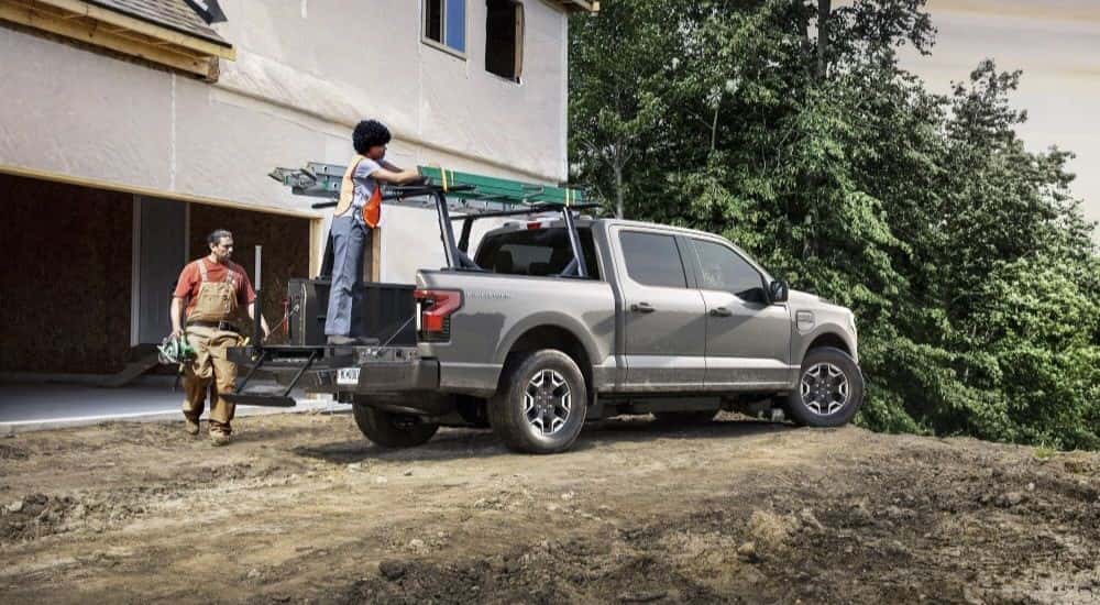 A grey 2023 Ford F-150 Lightning Pro parked near an unfinished house.