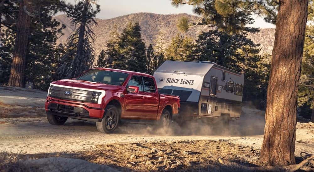 A red 2025 Ford F-150 Lightning towing a trailer off-road.