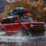 A red 2025 Ford Bronco Outer Banks off-roading in a stream