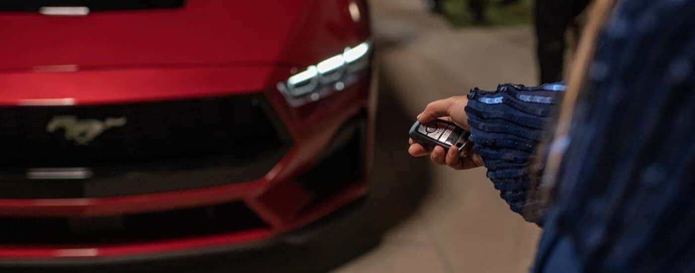 A person is shown using a keyfob near a red 2024 Ford Mustang after visiting a Ford dealer in San Leandro.