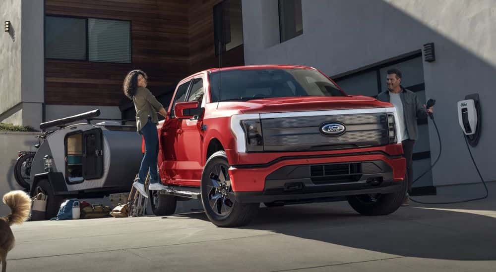 A red 2025 Ford F-150 Lightning towing a camper