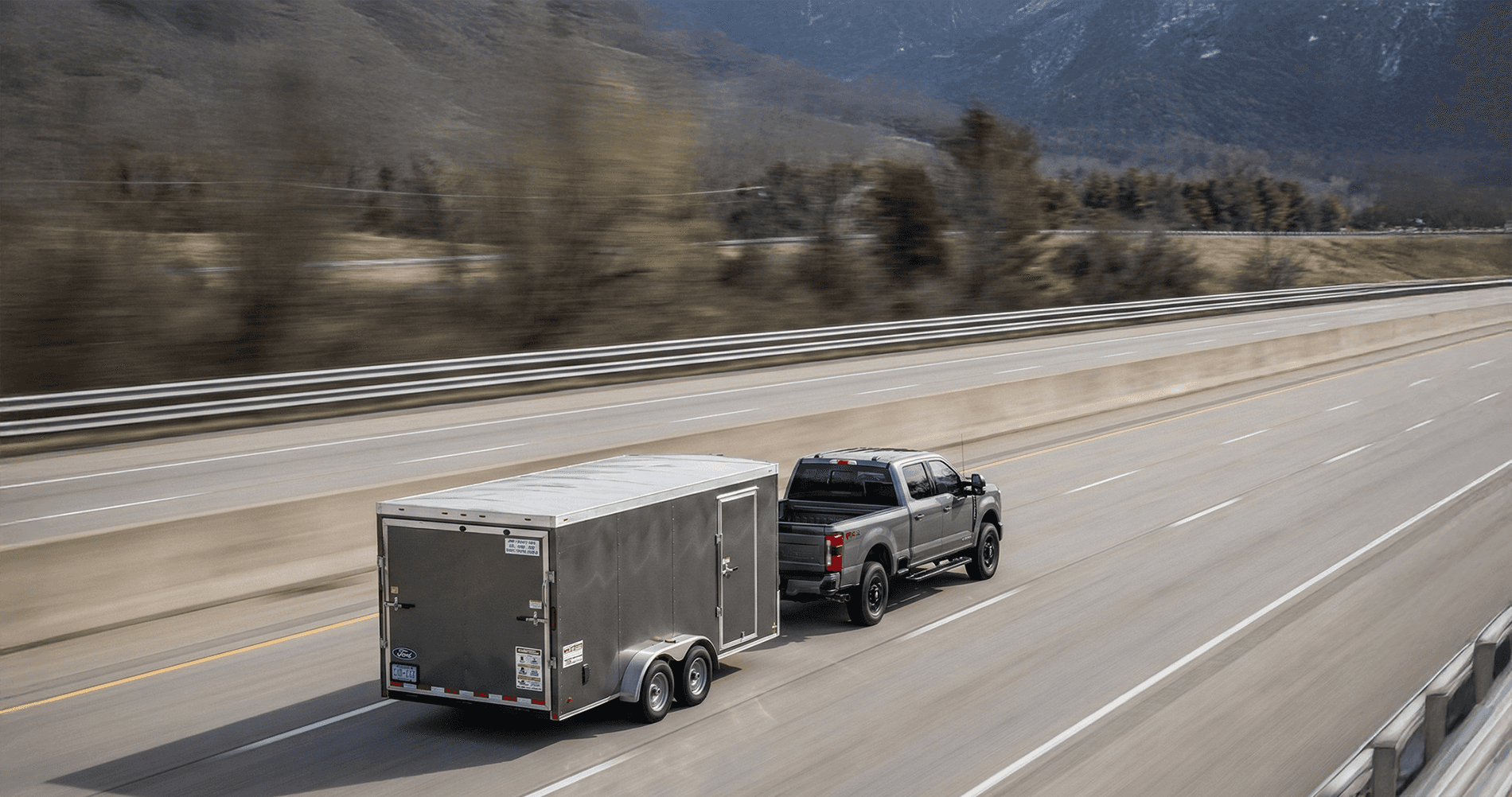 A Ford F‑250 Super Duty towing a large trailer on a dirt road, with dust rising behind the load and rolling hills and trees in the background, emphasizing the truck’s towing capability.