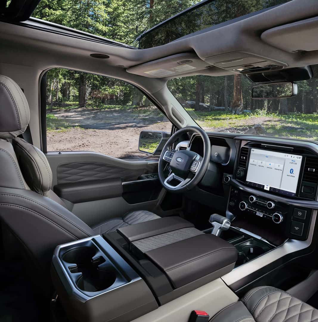 Ford F-150 interior showing front seats, center console with cupholders, large touchscreen infotainment system, digital instrument cluster, and panoramic sunroof above the cabin.