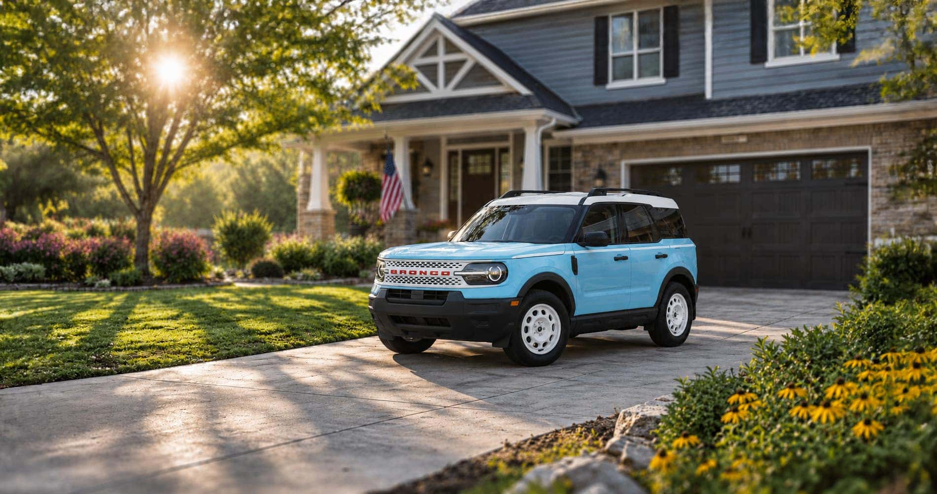 Light blue Ford Bronco Sport Heritage Edition parked in driveway at sunrise showcasing retro styling and white wheels.