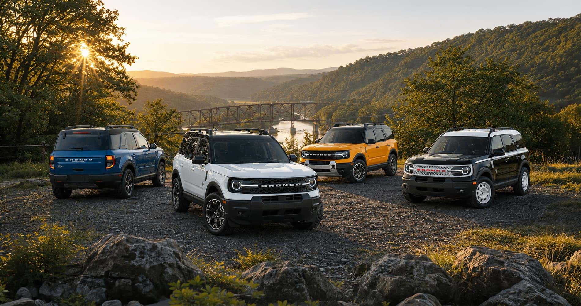 Four Ford Bronco Sport SUVs in blue white orange and black parked near river at sunset showcasing full trim range.