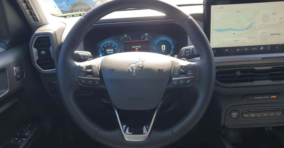 The interior of a 2025 Ford Bronco Sport featuring a digital instrument cluster, a large infotainment screen displaying navigation, and various control buttons on the steering wheel and center console.