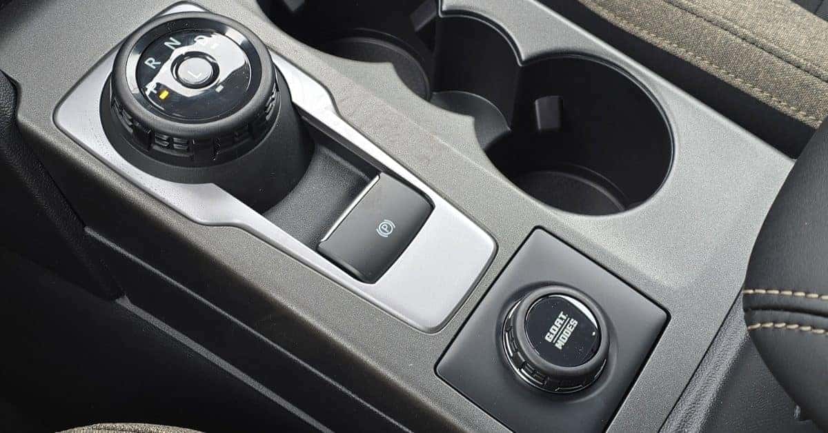 Close-up of the center console in a 2026 Ford Bronco Sport, featuring a rotary gear selector, electronic parking brake button, cupholders, and a 'G.O.A.T. Modes' drive selector dial for off-road terrain options.