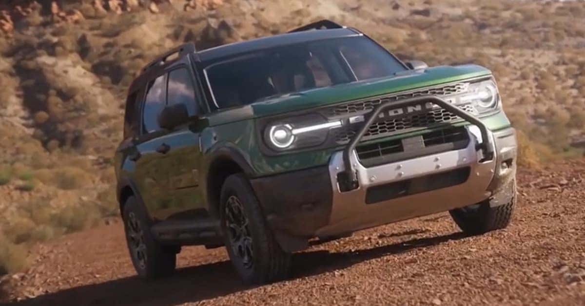 A green 2025 Ford Bronco Sport SUV navigating an uneven dirt trail in a rugged, arid landscape with hills and sparse vegetation, emphasizing its off-road capabilities.
