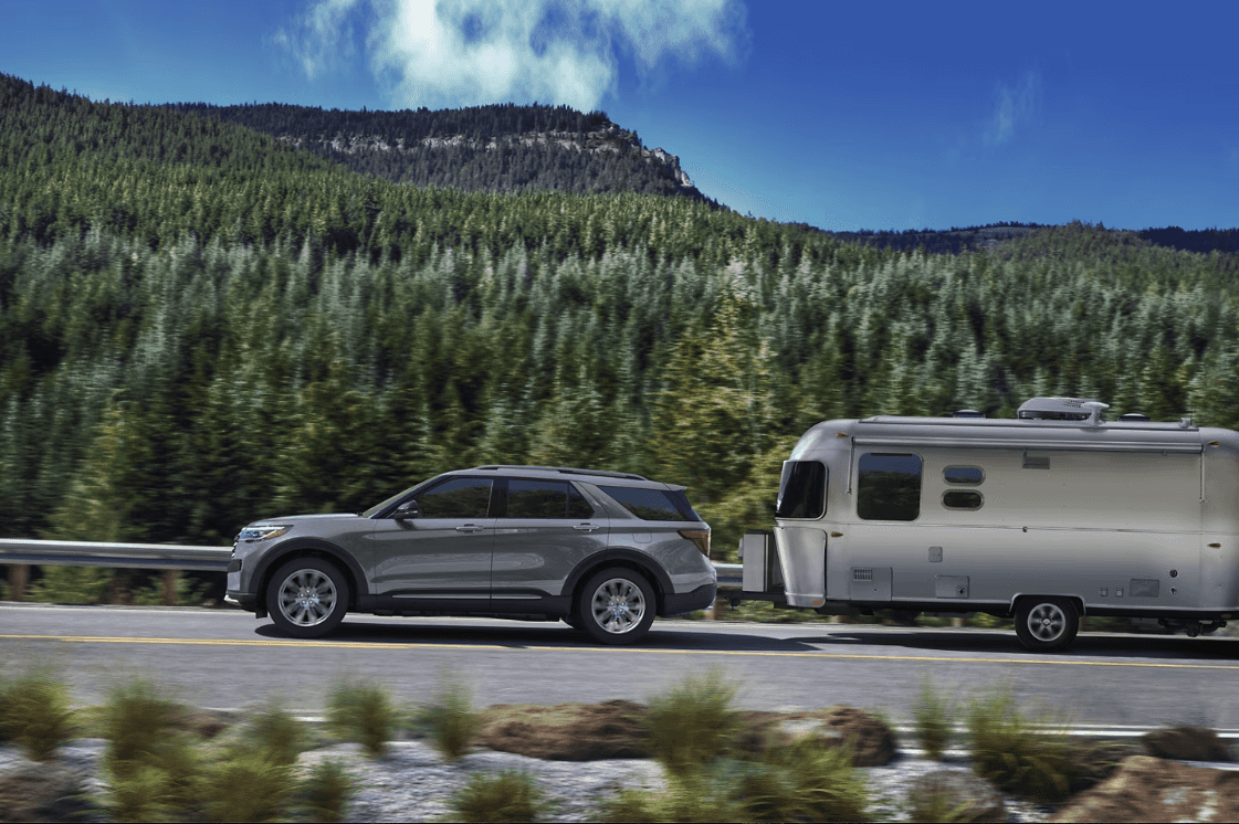 Side view of the 2025 Ford Explorer towing a trailer with trees and mountains in the background