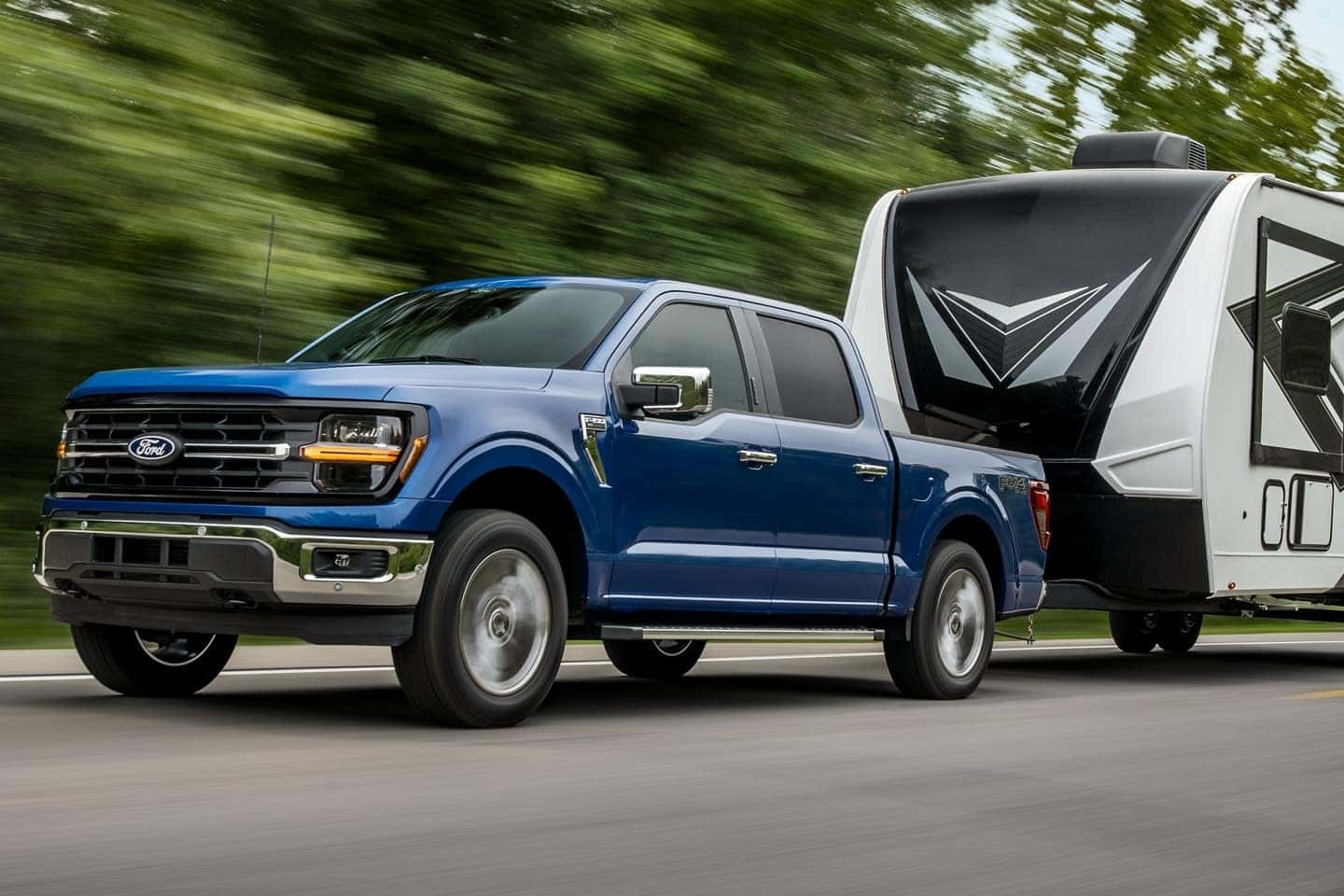Blue 2024 Ford F-150 driving down the road and hauling a trailer