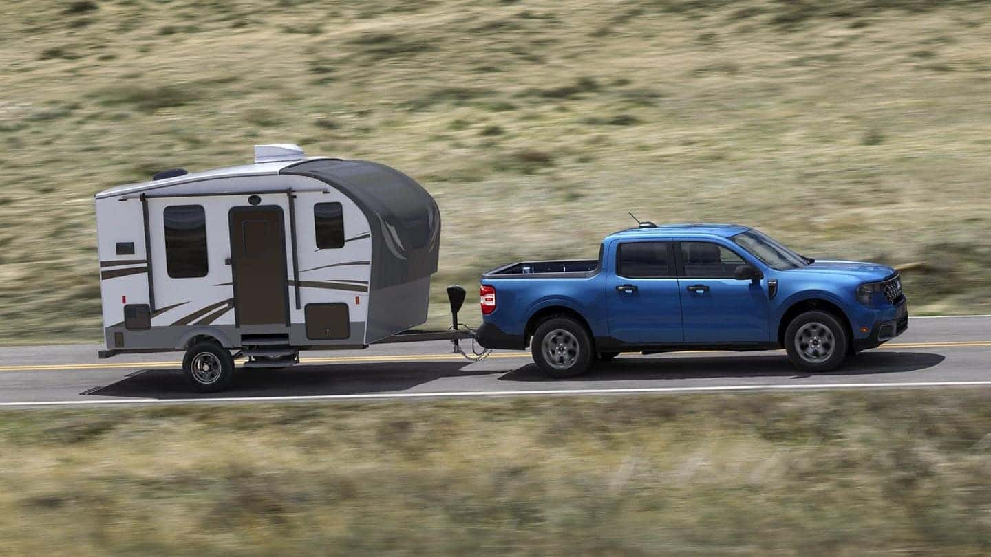 A blue 2025 Ford Maverick hauling a small trailer as it drives