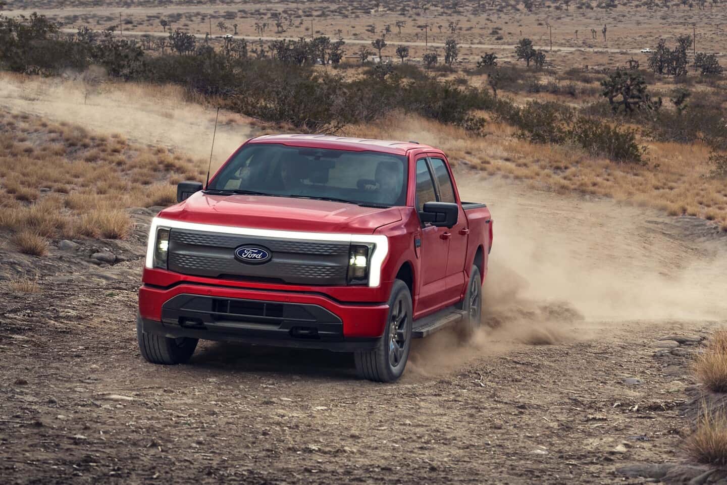 A red Ford F-150 Lightning driving on a dirt road