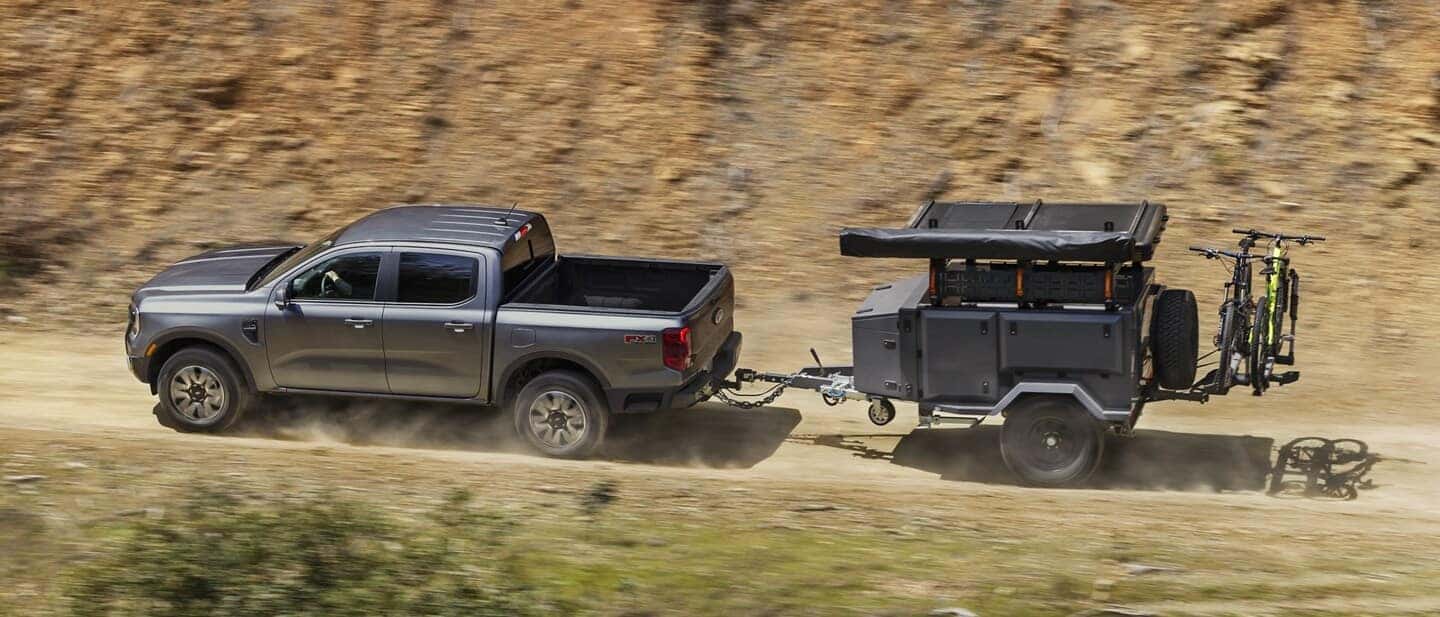 A silver 2025 Ford Ranger towing a small trailer through a desert