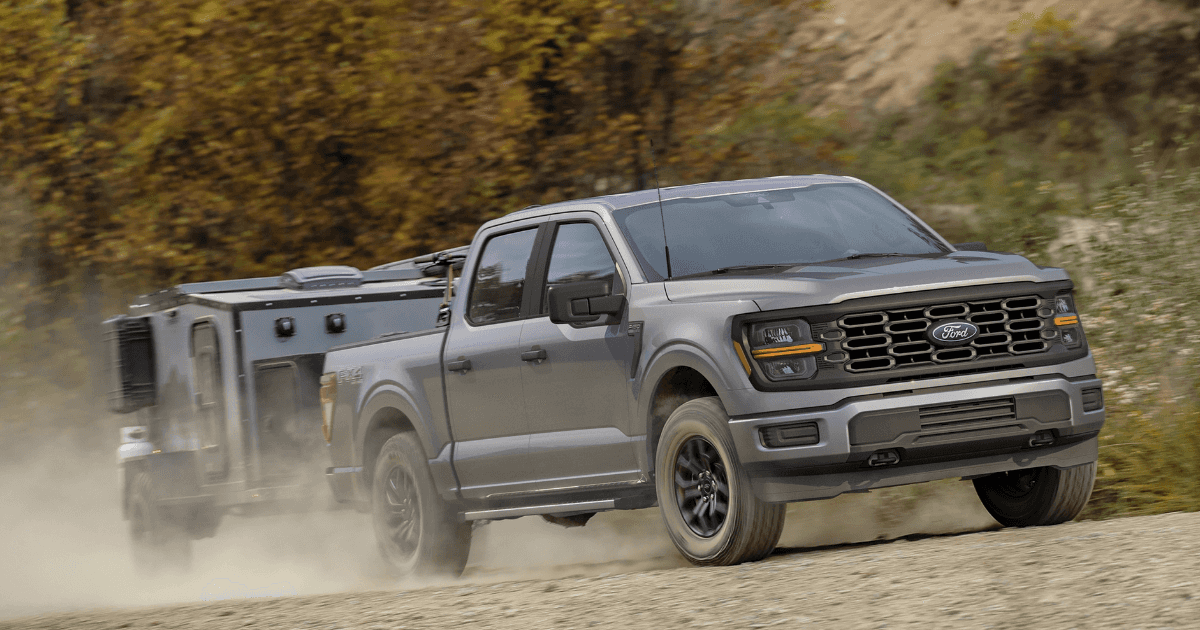 A gray Ford F150 hauling a trailer off-road up a hill.