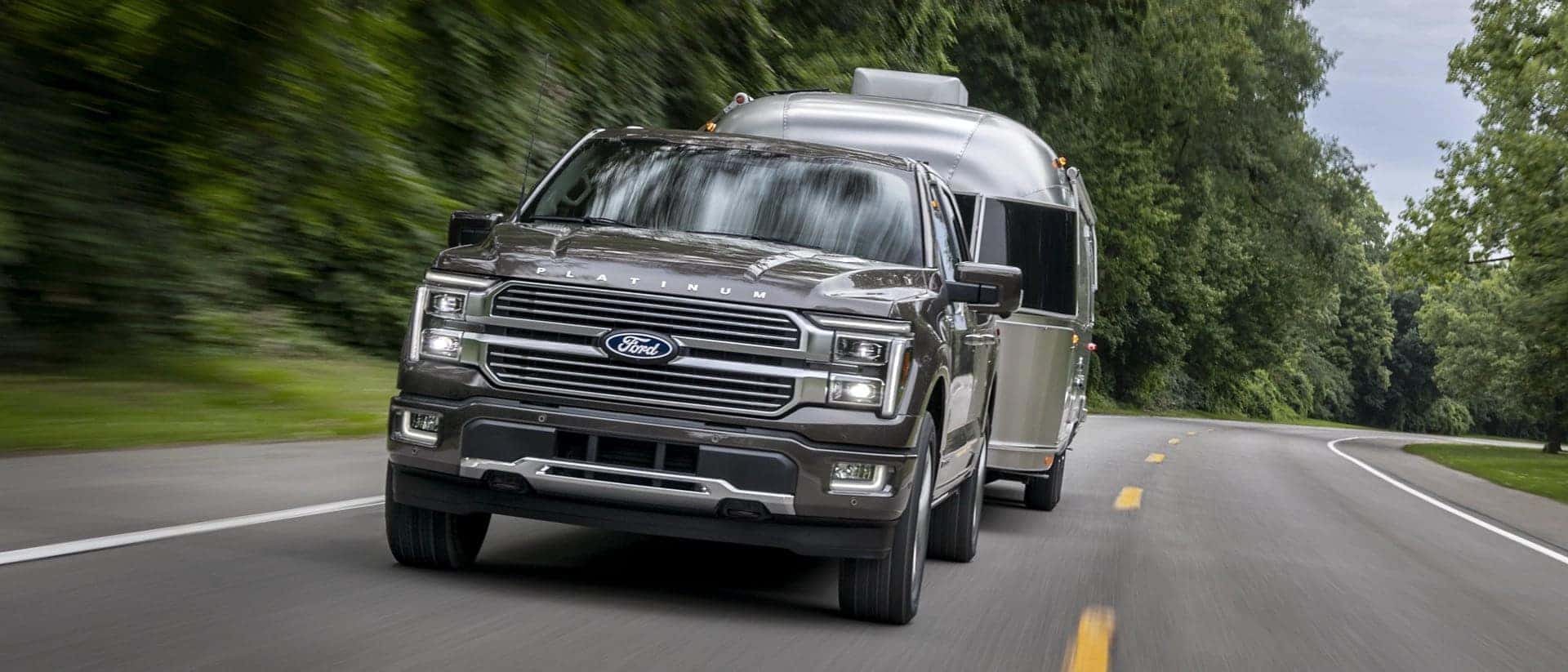 A front view of a gray Ford F-150 driving quickly while towing a trailer