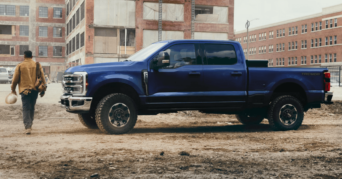A blue Ford Super Duty parked at a construction site with a worker walking in front of it