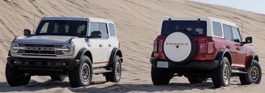 Two Ford Broncos side by side on sand dunes