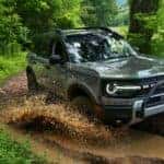 A light green Ford Bronco Sport driving off-road through mud