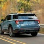 A light blue Ford Explorer driving by a forest in autumn