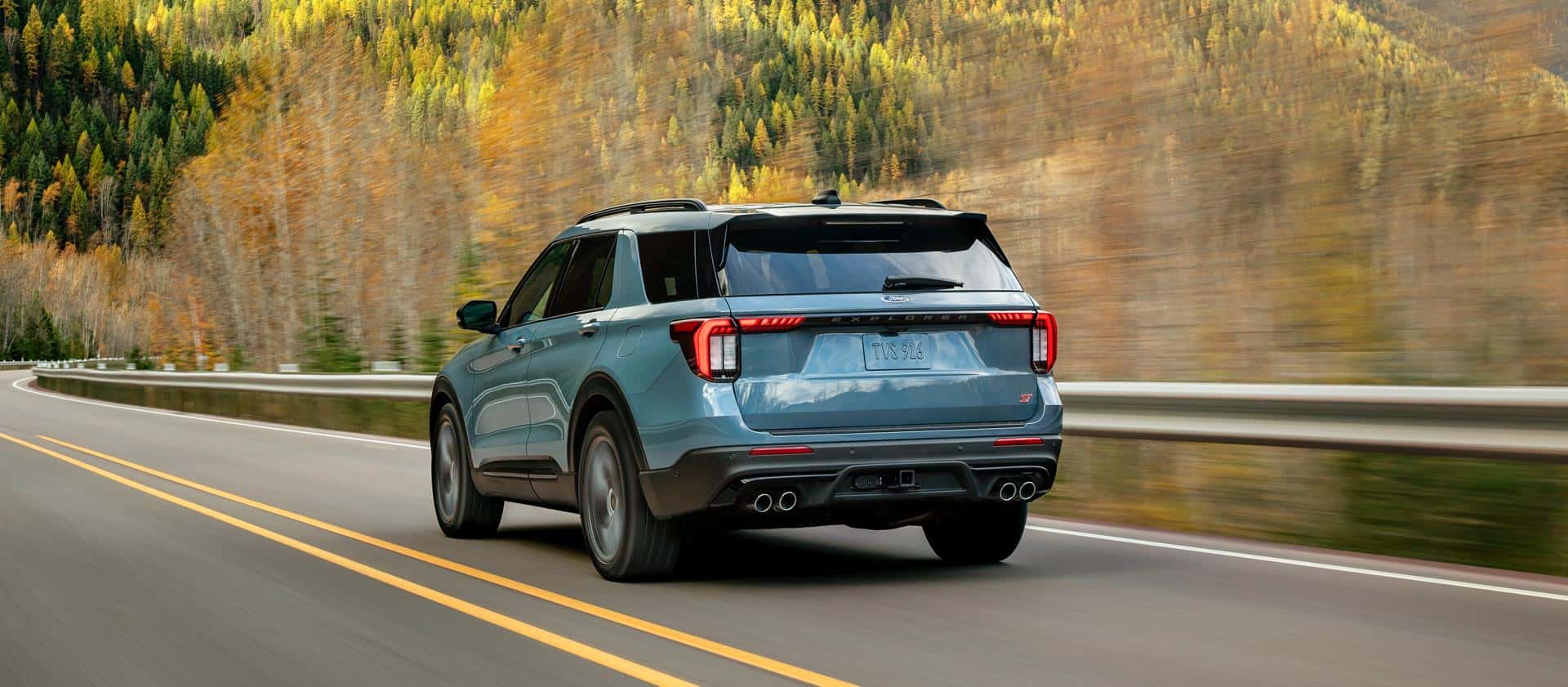 A light blue Ford Explorer driving by a forest in autumn