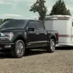 A black Ford F-150 hitched to a horse trailer on a ranch