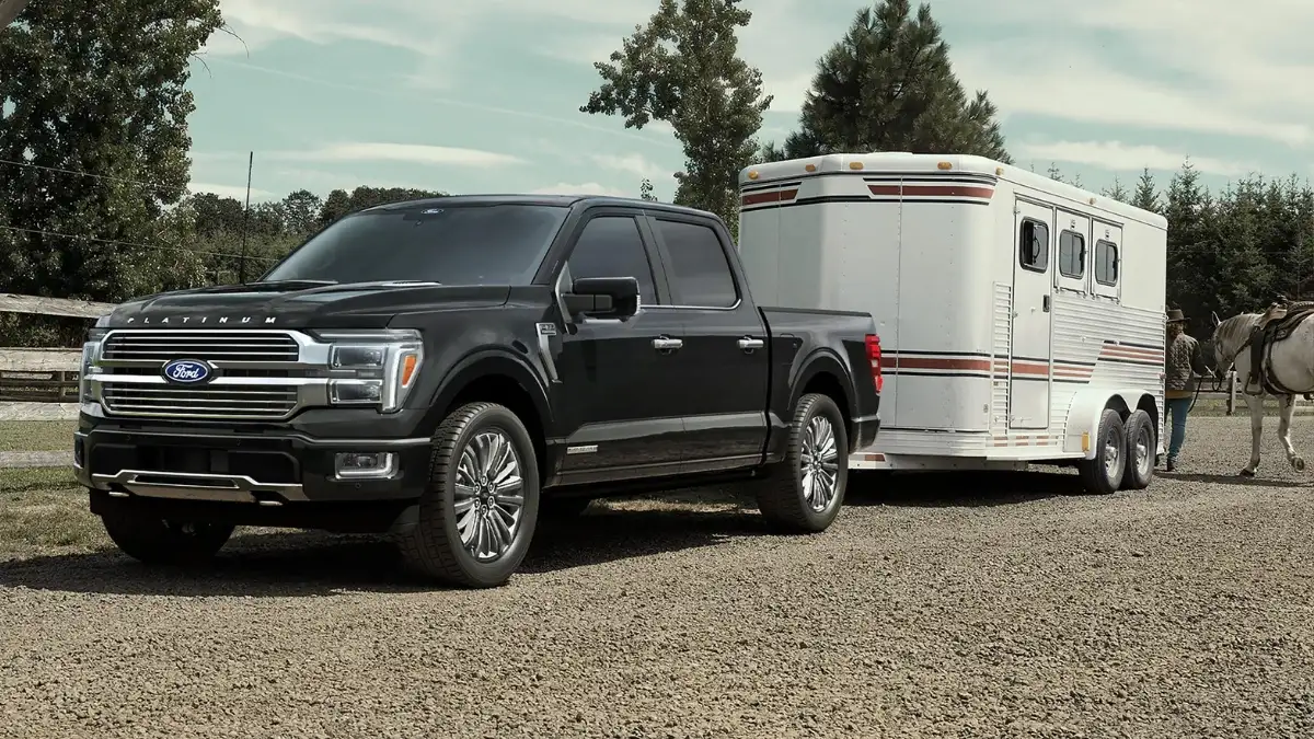 A black Ford F-150 hitched to a horse trailer on a ranch