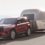 A red FOrd Explorer towing a trailer across a cliffside road by the ocean.