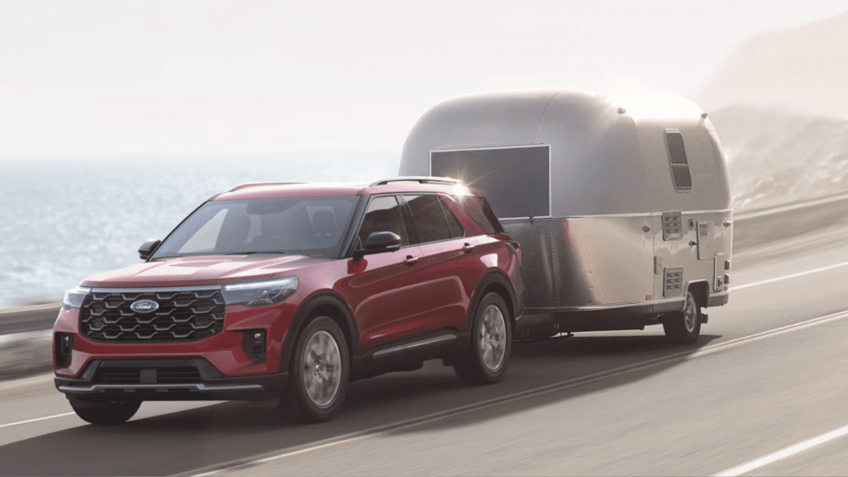 A red FOrd Explorer towing a trailer across a cliffside road by the ocean.