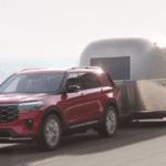 A red Ford Explorer driving on a cliffside road while towing a trailer