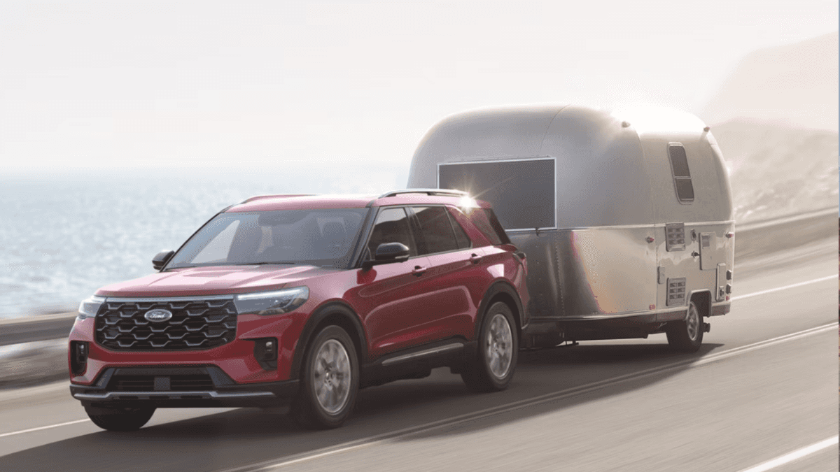 A red Ford Explorer driving on a cliffside road while towing a trailer
