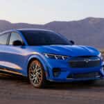 A blue car parked on a dirt road with a desert mountain range