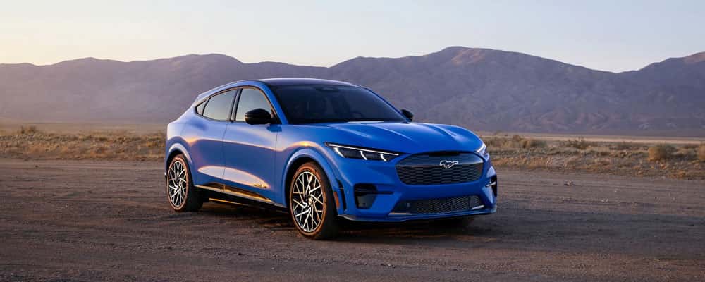 A blue car parked on a dirt road with a desert mountain range