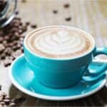A blue cup with a white foam in it next to coffee beans