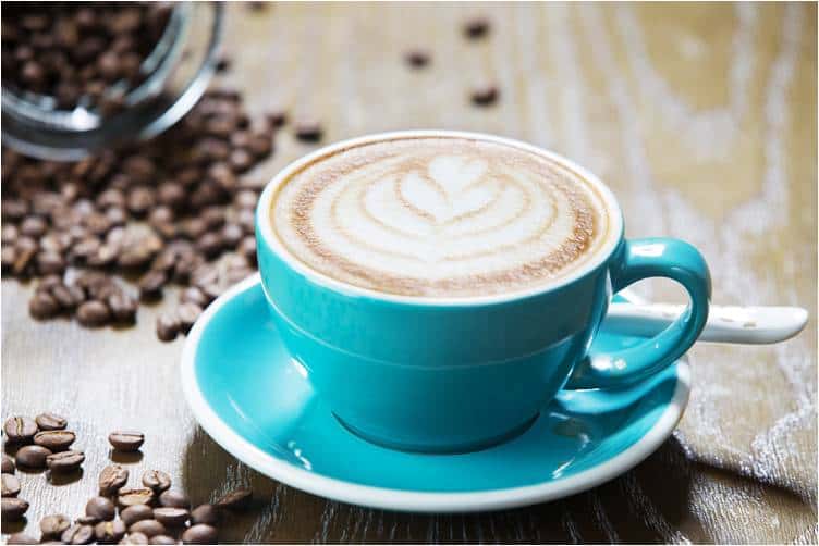 A blue cup with a white foam in it next to coffee beans
