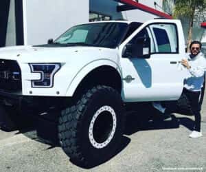 Man wearing white hoodie and black sweat pants getting into white Ford truck