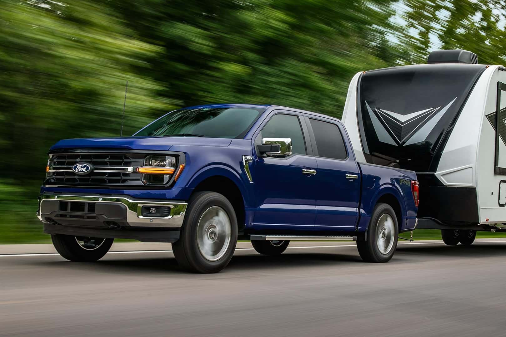A blue 2026 Ford F-150 driving down the road while towing a travel trailer