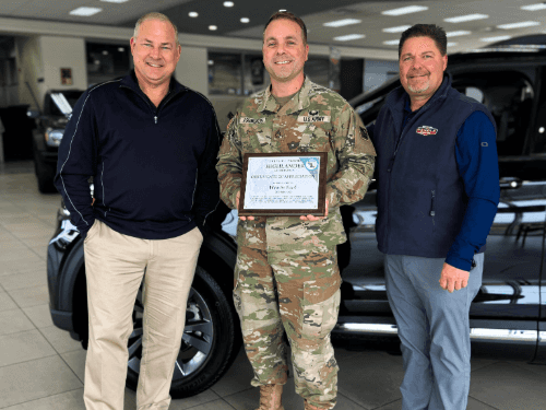Three people standing in front of a car holding a plaque.