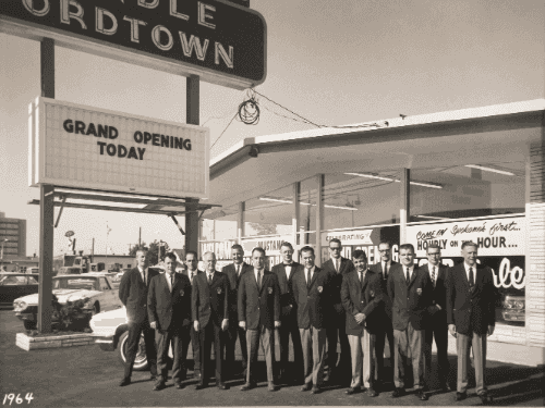 Chud and Dick Wendle standing with their sales team in front of the new Northtown dealership during its 1964 Grand Opening.
