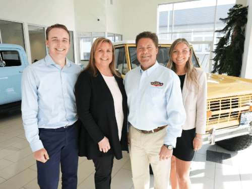 A 2023 portrait of the Wendle family standing showroom in front of a vintage yellow Bronco.