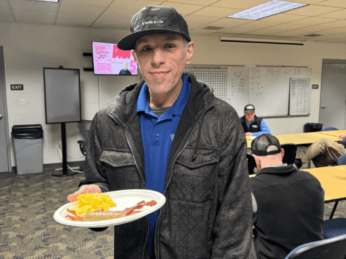 A Wendle service staff smiling and holding plates of food at a staff appreciation breakfast. The team is gathered in the dealership breakroom for a community-building meal.