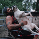A large white dog sitting with a man in a chair.