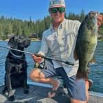 Black dog sitting in a boar with a man holding a fish.