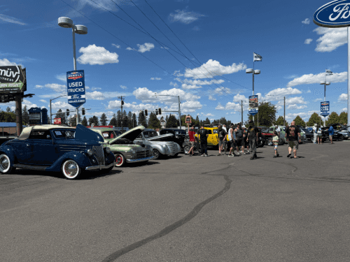 Classic vintage cars, including a blue convertible and green sedan, on display at the Wendle dealership car show with many visitors..