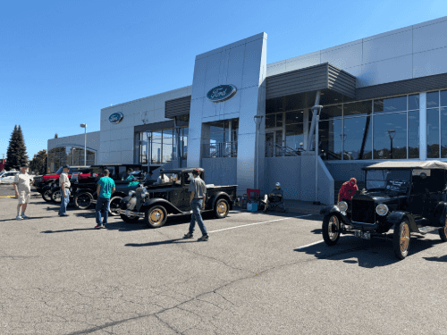 Vintage Ford Model T and Model A cars on display directly in front of the modern, silver Wendle Ford dealership showroom.