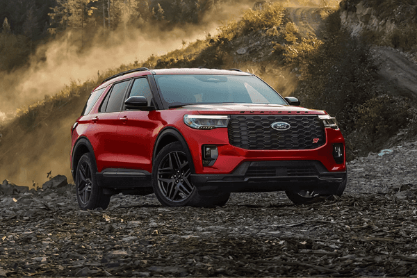 A red Ford Explorer ST parked on a rugged, rocky mountain trail with dust rising in the background.