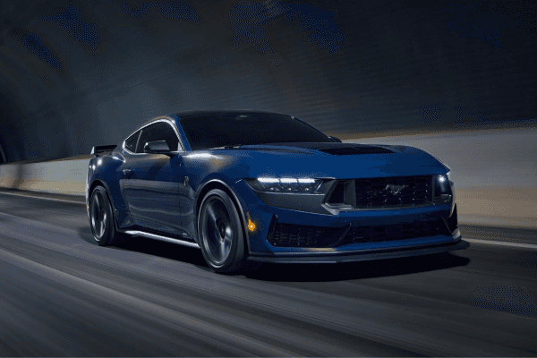 A dark blue Ford Mustang coupe speeding through a dimly lit tunnel with its headlights on and motion blur on the road.